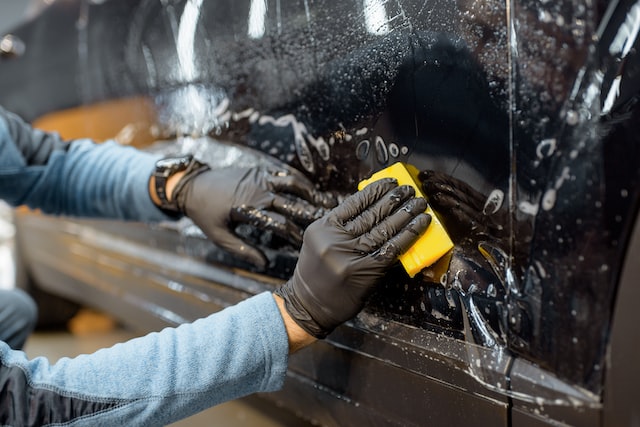 worker sticking anti-gravel film on a car body